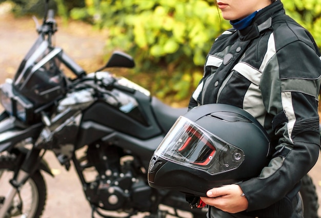 Meisjesmotorrijder houdt een beschermende helm in haar handen op de achtergrond van een wazige motorfiets.