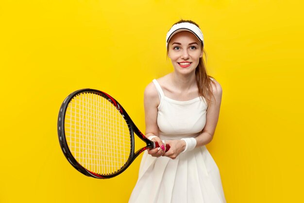Meisjestennisser in sportkleding die tennisracket op gele achtergrond houdt en glimlacht