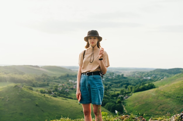 Meisjestoerist in stijlvolle kleding staat op de berg met een prachtig groen landschap en kijkt met een serieus gezicht naar de camera Zakupne Tovtry