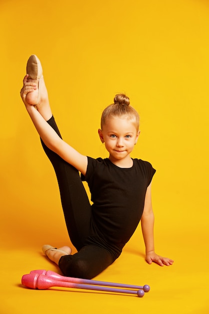 Meisjesturner leidt met gymnastiekclubs op gele achtergrond op. professionele sporten voor kinderen. Mooi tienermeisje dat ritmische gymnastiekoefeningen doet