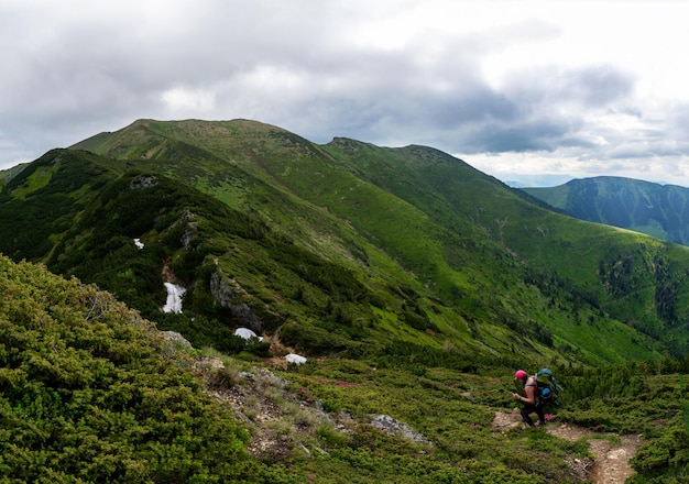 Meisjeswandelaar met een rugzak staat op een rots in de bergen Trekkingsleven Wandeling door de Karpaten Groene berghellingen en bloeiende rododendron