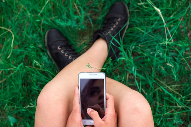 meisjeszitting met telefoon in handen op gras hoogste mening