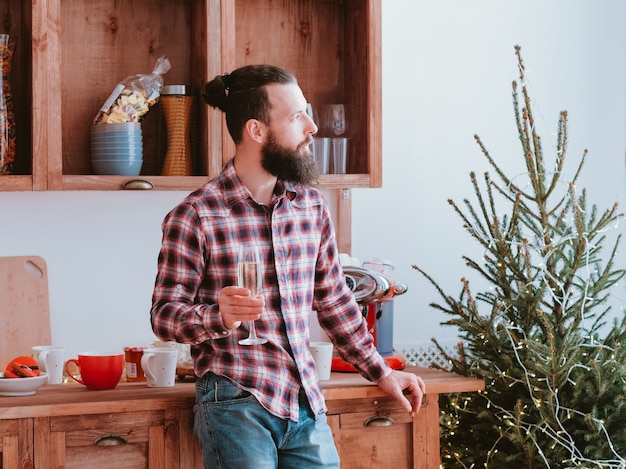 Melancholie van Kerstmis. Nadenkend hipster kerel champagne drinken in de keuken, kijkt uit raam