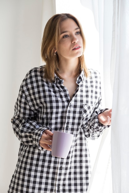 Melancholisch meisje dat koffie drinkt en uit het raam kijkt