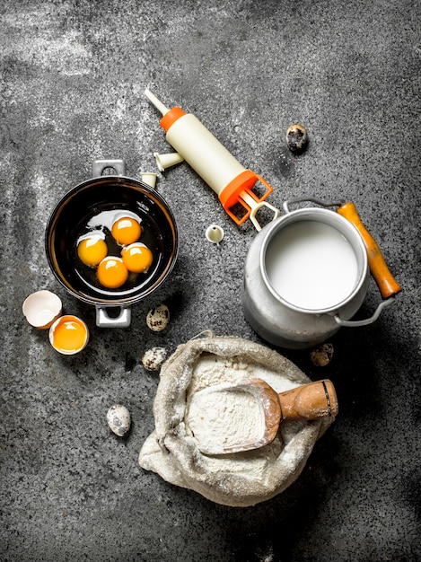 Melk, bloem, eieren en suikergoedspuit voor cake op rustieke lijst.