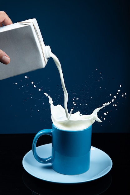 Melk gegoten in een glas met splash op donkerblauwe achtergrond.