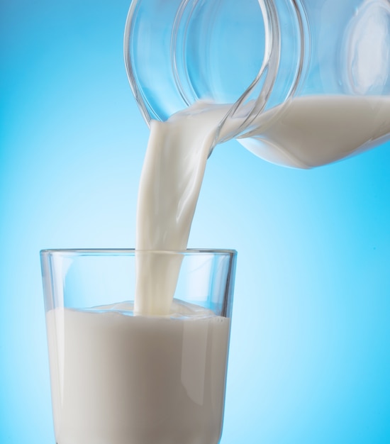 Melk gieten van kruik in een glas op blauw