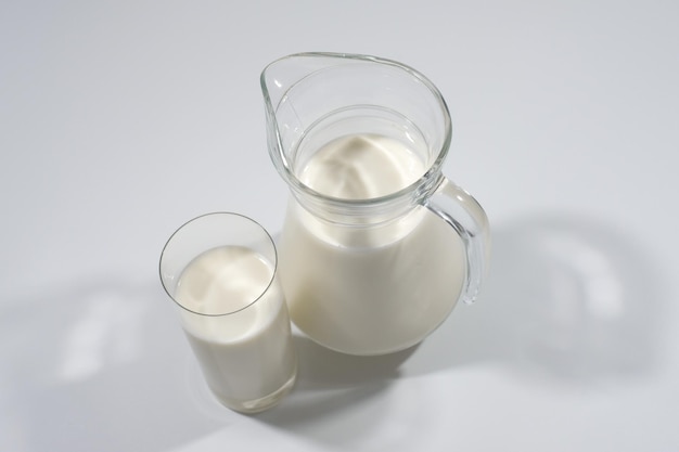 Melk in een glas met een kan op een grijze achtergrond Zijaanzicht Melkproduct