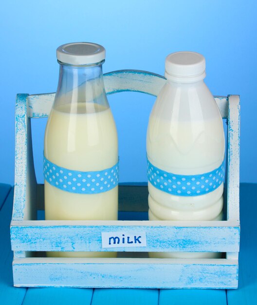 Foto melk in flessen in houten kist op blauwe houten tafel op blauwe achtergrond