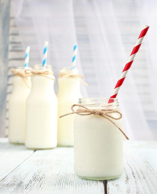 Foto melk in flessen met papieren rietjes op tafel