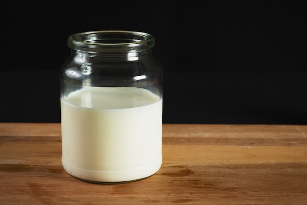 Melk in glazen fles op houten voet met zwarte ondergrond.