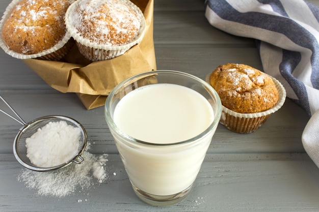 Melk in het glas en zelfgemaakte cupcakes met poedersuiker op grijs hout