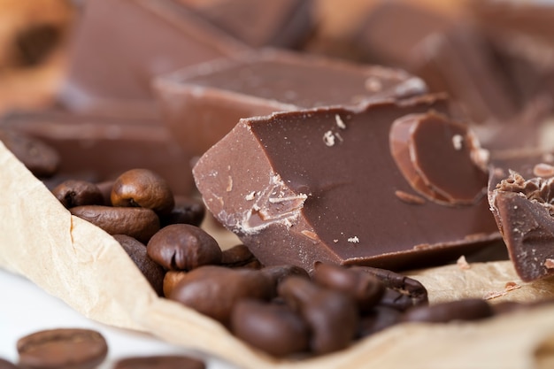 Foto melk- of bittere chocolade in een groot aantal stukjes gebroken, chocolade gemaakt van suiker en cacao, heerlijke stukjes chocolade gemaakt van cacaopoeder