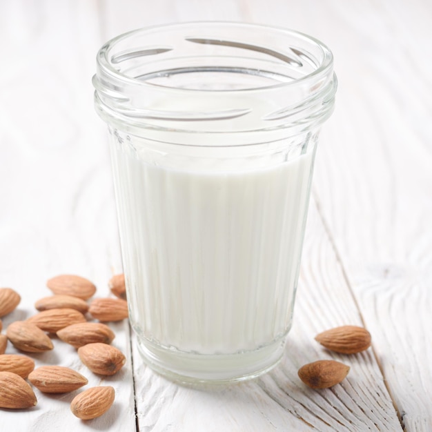 Melk of yoghurt in glazen pot op witte houten tafel met amandelen opzij