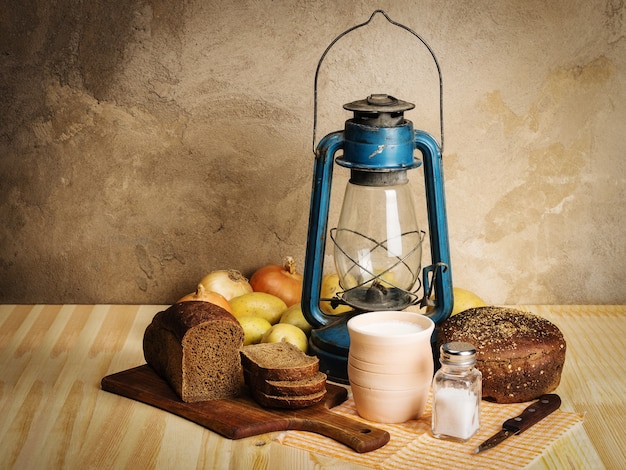 melk roggebrood snijplank zout uien aardappelen mes en kerosine lantaarn op houten tafel