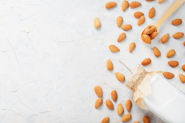 Melk van biologische amandelen in een transparante fles met een verstrooiing van zaden en een houten lepel op een lichte achtergrond