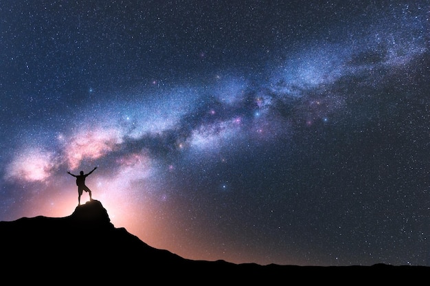 Melkweg en gelukkige man met rugzak op de bergtop 's nachts Silhouet van man met opgeheven arm op de heuvelhemel met sterren geel licht in Nepal Galaxy Space landschap met melkweg