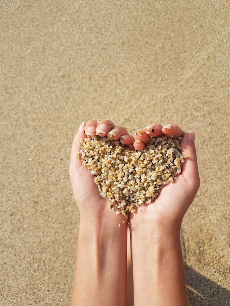 Foto cuore morbido che modella le mani femminili sopra il mare e la spiaggia.