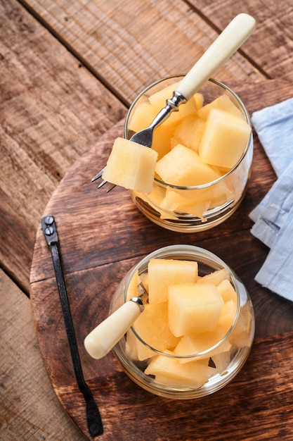 Meloen. Stukjes verse meloen voor het maken van fruitdessert in glas op een oude houten ondergrond. Bespotten. Bovenaanzicht.