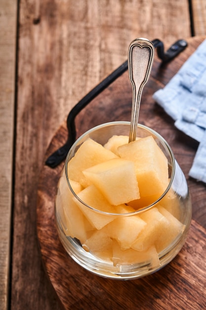 Meloen. Stukjes verse meloen voor het maken van fruitdessert in glas op een oude houten ondergrond. Bespotten. Bovenaanzicht.