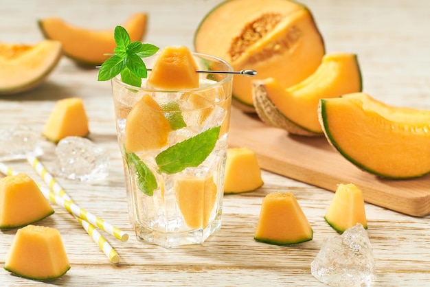 Meloenlimonade met ijs en munt in een glas op een houten tafel. Meloendrank in glazen met meloenplakken.