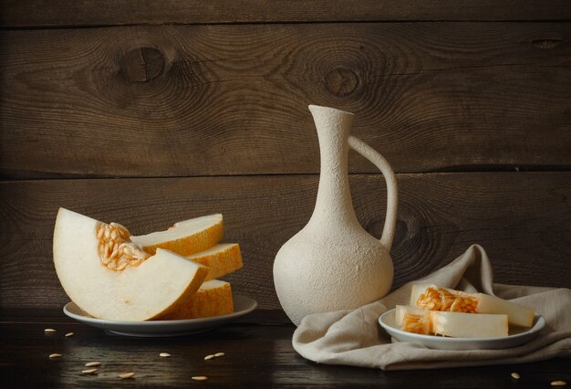 Meloenschijfjes op tafel, kruik, houten achtergrond