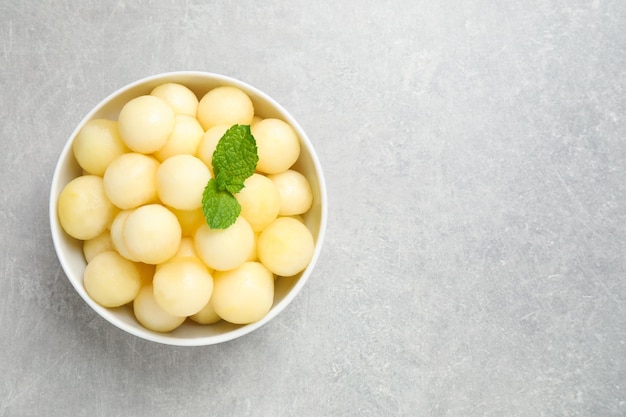 Melon balls and mint in bowl on light grey table top view space for text