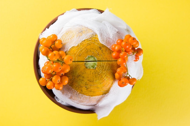 Melon and rowan berries on yellow background melon in form of mummy in gauze bandage funeral vegetables in egyptian tradition surreal food concept