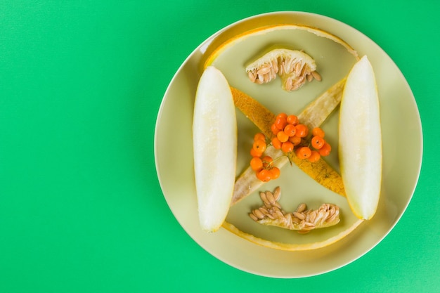 Melon slices melon seeds and skins on a green plate Melon and rowan berries on green background Vegetarian healthy food Top view Copy space