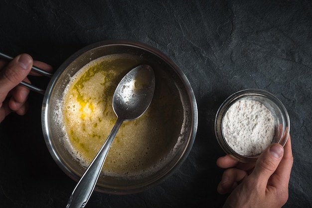 Photo melted butter in a ladle and a bowl of flour in a hand