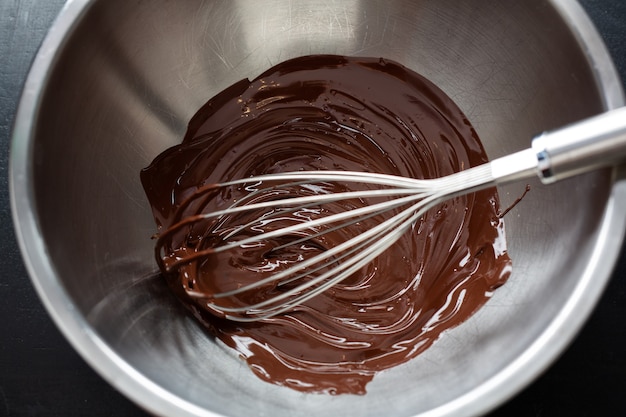 Melted chocolate in pot with chocolate pieces around on dark surface