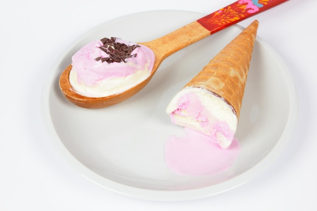 Melted ice cream with waffle cone and wooden spoon on white plate isolated on white background Pink ice cream on a white plate closeup