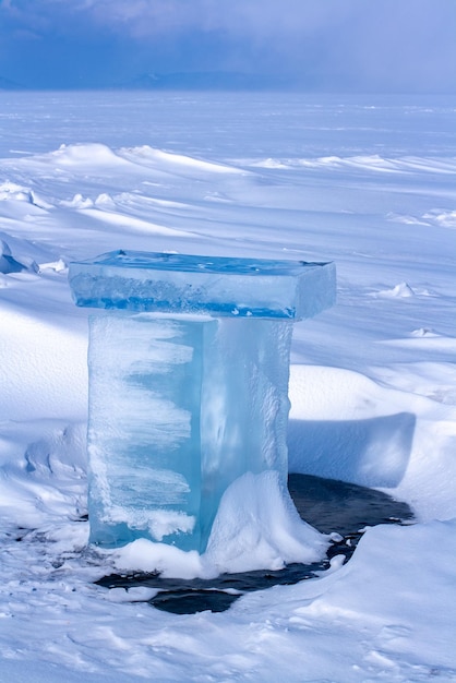 Melted in the sun chunks of ice in the snowy hummocks on the lake Baikal The ice is covered with snow Winter landscape Focus on ice blurred background Horizontal