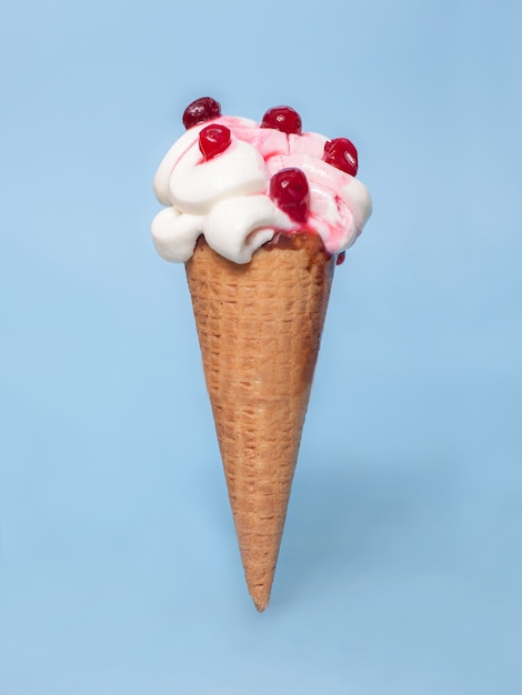 Melting ice cream cone with cranberries topping isolated on blue background