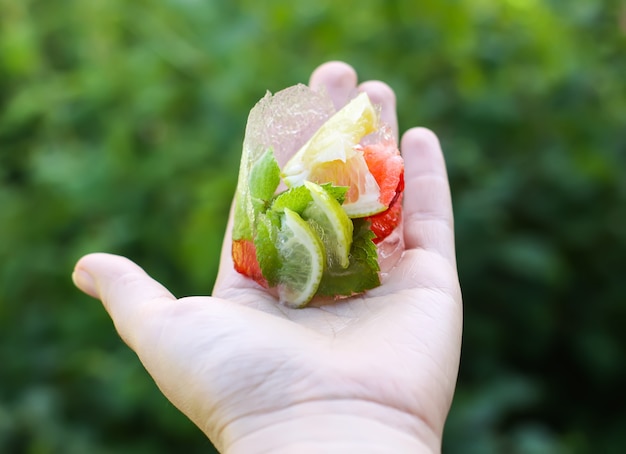 Melting ice cube with strawberry, lemon and fresh green mint leaves in a hand