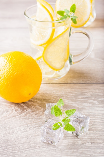 写真 アイスキューブ、新鮮なミントの葉、木製のテーブルの上のグラスにレモンと水を溶かす