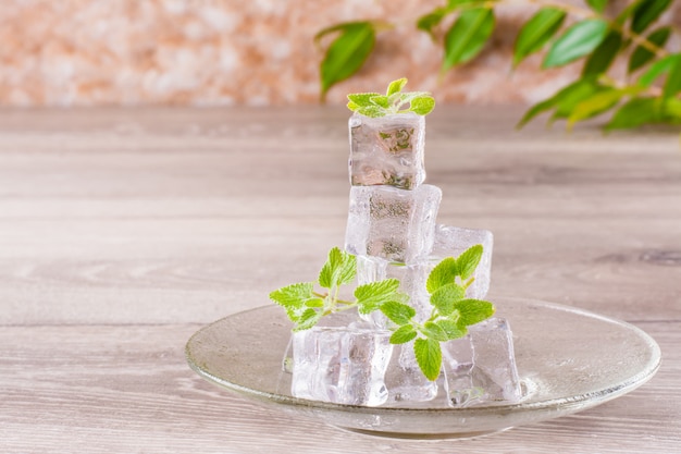 Melting ice cubes and mint leaves on a saucer on a wooden table