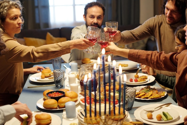 Photo members of large jewish family clinking with wineglasses over served table