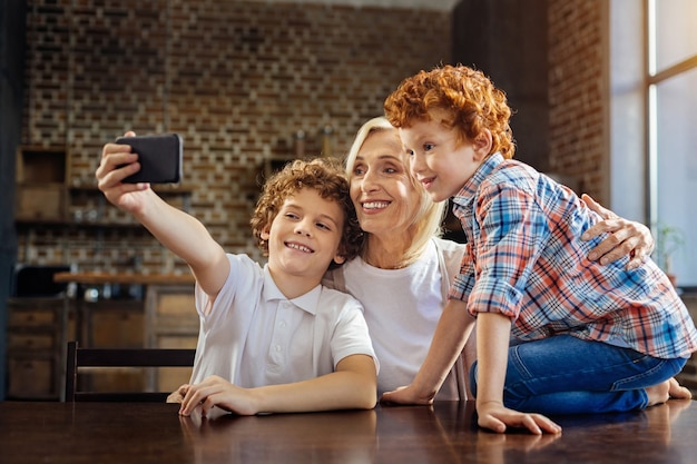 Memorable moment. Side view on a happy family members meeting at a dinner table and grinning broadly while taking a self portrait picture on a smartphone.