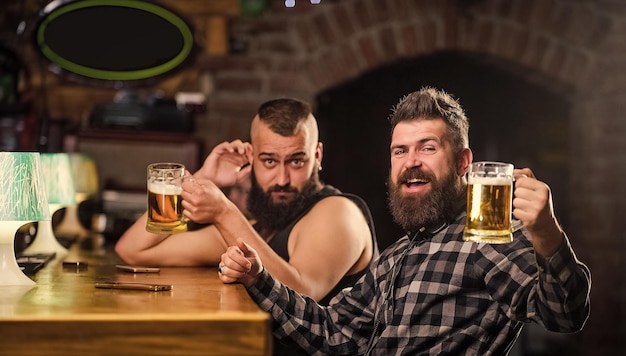 Men drunk relaxing having fun Alcohol drinks Friends relaxing in pub with beer Refreshing beer concept Men drinking beer together Hipster brutal man drinking beer with friend at bar counter