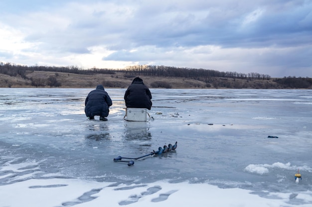 Men fishing on ice winter fishing on a frozen river in the evening at sunset