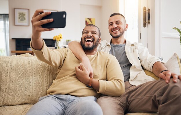 Men gay couple and funny selfie in home living room bonding and laughing together People lgbtq and profile picture happy memory and smile on social media in love care and hug on sofa in lounge