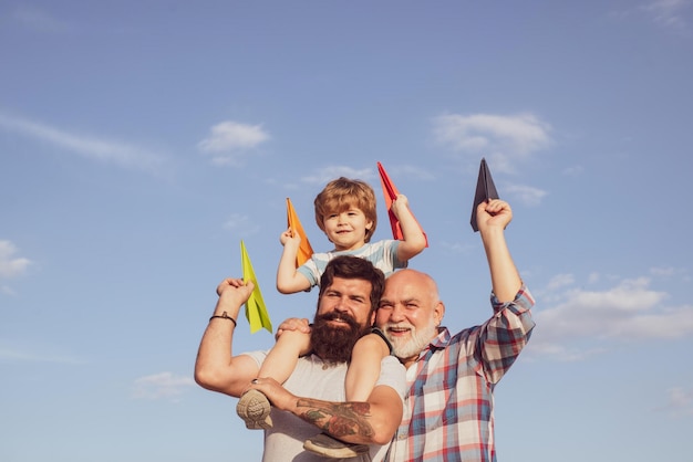 男性世代の祖父の父と孫がカメラを見て抱きしめ、笑顔で幸せな父の肖像画が息子にピギーバックを肩に乗せて見上げる