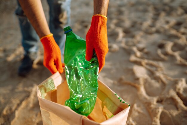 男性の手は海のビーチでペットボトルを収集します。保護手袋を着用したボランティアがペットボトルを回収します。