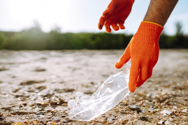 Men hand collects plastic bottle on sea beach.