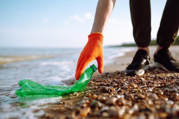 Men hand collects plastic bottle on sea beach.