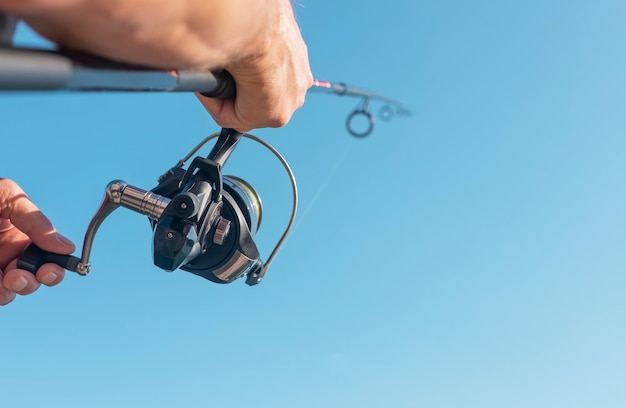 Mani degli uomini che tengono la canna da pesca volante o il pescatore sopra il cielo blu chiaro