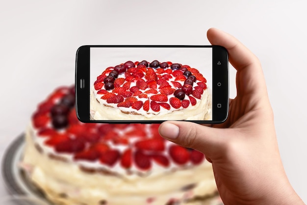 Men hands takes photography of food on table with phone Strawberry cake