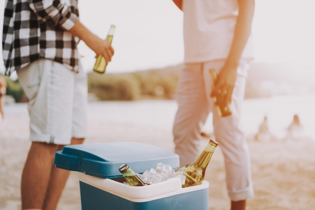 男性は夕日の光の中でビーチパーティーでビールを持っています