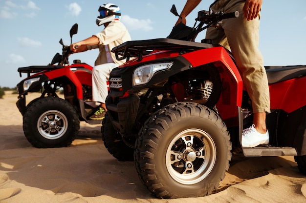 Men in helmets and glasses ride on atv in desert